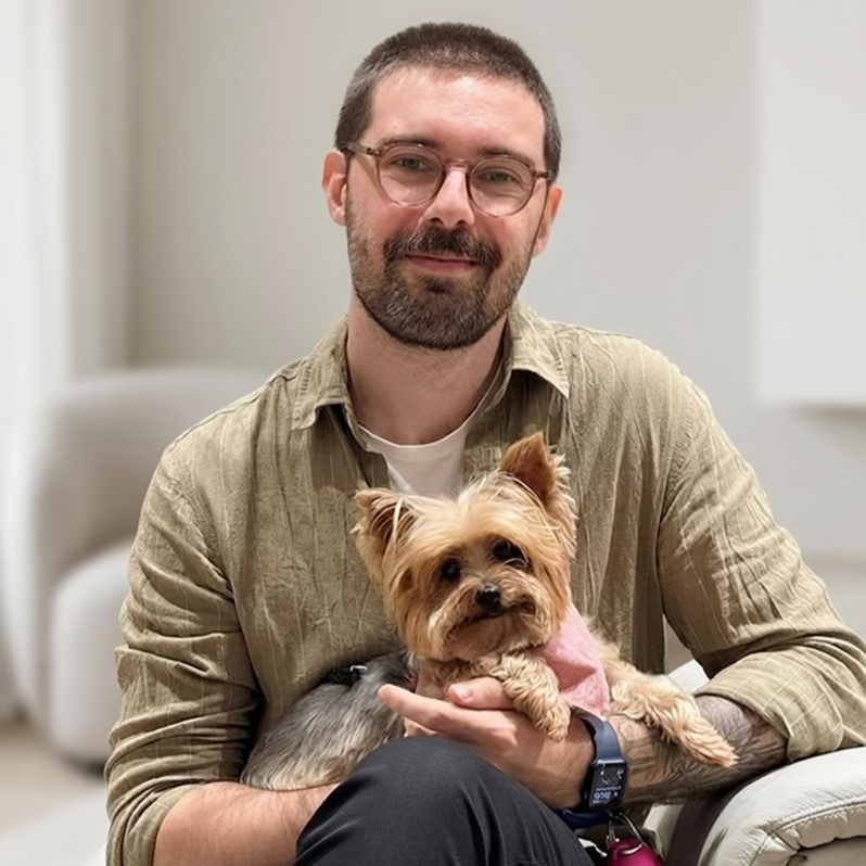 a photo of a man with short hair, glasses with a small dog on his arms.